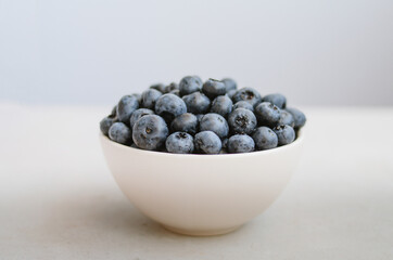 Freshly picked blueberry in white bowl on dark blue background. Handful of sweet ripe berries close up 