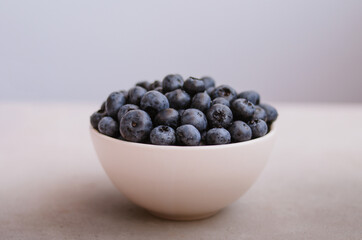 Fresh ripe blueberry in ivory bowl on blue background close up