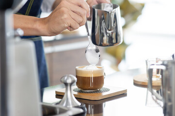 Close up hand of Asian barista man stands intentionally making hot cappuccino coffee cappuccino to serve customers in the coffee shop..
