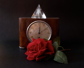 Vecchio orologio, cristallo e rosa rossa su di un tavolo