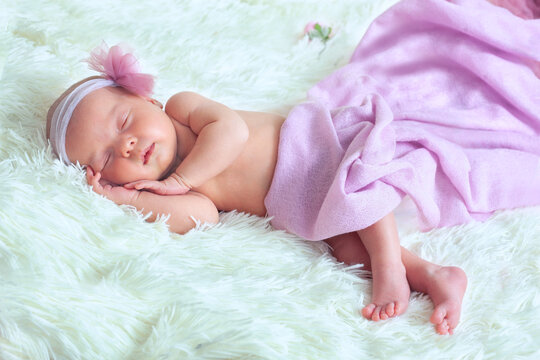 A newborn photo of a little girl sleeping on a soft white fluffy blanket in a pink Tu-Tu skirt and a headband