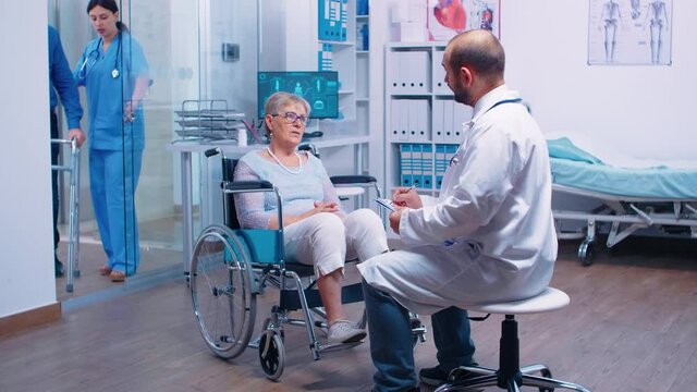 In busy modern private recovery clinic or hospital doctor is talking with disabled patient in wheelchair while nurse is bringing a man with walking disabilities in. Health care medicine support