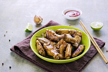 Fried Chinese style chicken wings sprinkled with white sesame seeds in a green ceramic bowl on a gray concrete background. Grill, barbecue recipes.