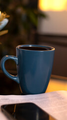Evening coffee. Blue cup with coffee, open book and mobile phone, evening light, sunset, dusk. Atmospheric, cozy evening in the garden, green leaves, conversation. Warm light, blur bokeh.