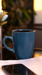 Evening coffee. Blue cup with coffee, open book and mobile phone, evening light, sunset, dusk. Atmospheric, cozy evening in the garden, green leaves, conversation. Warm light, blur bokeh.
