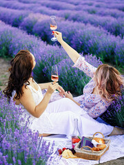 two women drink wine in lavender field, picnic, blurred background