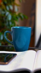 Evening coffee. Blue cup with coffee, open book and mobile phone, evening light, sunset, dusk. Atmospheric, cozy evening in the garden, green leaves, conversation. Warm light, blur bokeh.