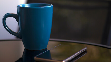 Evening coffee. Blue cup with coffee, open book and mobile phone, evening light, sunset, dusk. Atmospheric, cozy evening in the garden, green leaves, conversation. Warm light, blur bokeh.