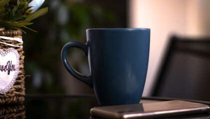 Evening coffee. Blue cup with coffee, open book and mobile phone, evening light, sunset, dusk. Atmospheric, cozy evening in the garden, green leaves, conversation. Warm light, blur bokeh.