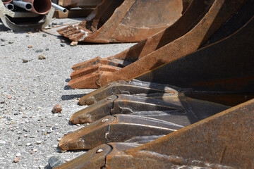 Baggerschaufeln auf Asphaltplatz, drei Schaufeln mit Baggerzähnen, metallene Gegenstände als grafische Elemente