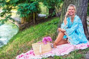 Naklejka na ściany i meble woman in her 40s sitting on pink blanket at a river