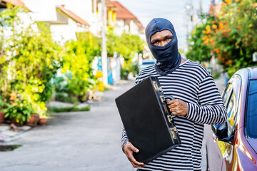 The male thief wears a black and white striped shirt and wears a black mask, smiling happily after...