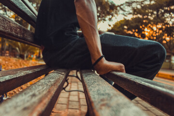 Jovem sentado no banco do parque apoiando as mãos