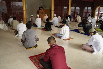 Muslim men are sitting inside the mosque maintaining social distancing and wearing masks while listening to lectures according to health protocols.