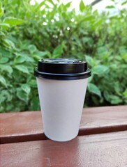White paper coffee cup disposable for take away or to go, at wooden table and green nature background, copy space for text or logo. Street coffee, top view.