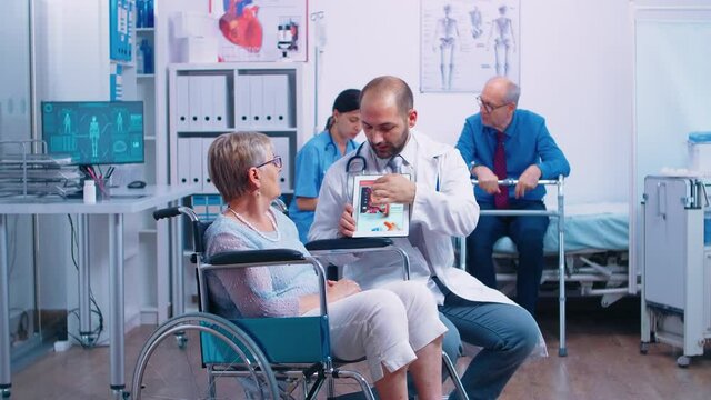 Medical stuff presenting a booklet with arrhythmias and other heart related disease to senior woman in wheelchair into a recovery clininc. Health care, medical advice and rehabilitation