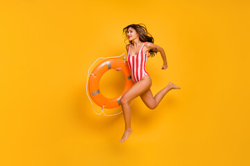 Full size profile photo of beautiful lady beach pool jumping into water lifeguard carry orange buoy save drowning person wear white red striped bodysuit isolated yellow color background