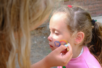 Artist painting a rainbow on girl's face. face are or face painting. festive make-up for kids....