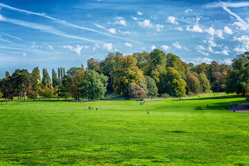 Bright green field on a sunny day against a blue sky. Resting people. Space for text.