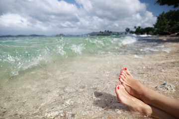 Shapely female legs with red nails  close-up on the beach in the clear water in Caribbean sea in Mexico.Travel concept.Vacation.