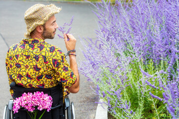 handsome man in wheelchair smelling purple flowers outdoors