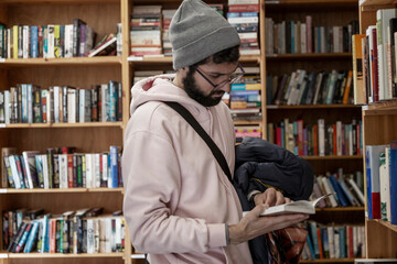 Young man in a bookstore. A brunette with glasses and a hat holds a book in her hands. Education, science and knowledge.