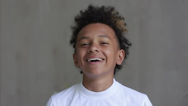 Portrait of African American boy is smiling and laughing in front of camera at home interior spbi. Handsome child looking forward with smile and positive emotions while standing in light room
