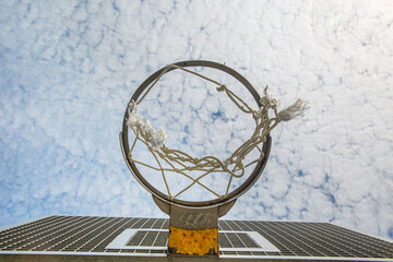 A broken basketball net dangles from a hoop attached to a metal backboard. Sunny day and clear blue...