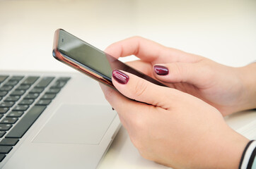 Female hands with bright color nails hold a smartphone against the background of a laptop keyboard. The symbol of modern communication is the Internet and the mobile network.