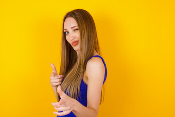 Hey you, bang. Joyful and charismatic good-looking emotive woman with blond curly haircut winking and pointing with finger pistols at camera happily and cheeky posing over white wall