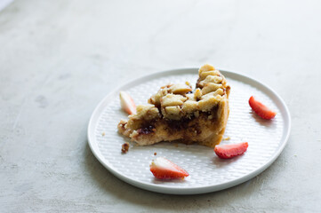 Piece of homemade cookie dough tart with strawberry jam and ricotta, with sliced strawberries on the light grey plate