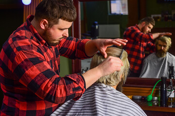Hipster client getting haircut. Professional hairstylist in barbershop interior. Barber and client. Barber works hairstyle for bearded man barbershop background. Guy with long dyed blond hair