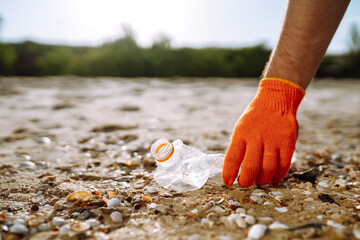 Men hand wearing protective gloves collects bottle plastic on sea beach. Problem of global plastic pollution of the Earth.