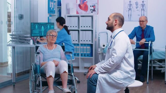 Doctor is using augmented reality to better understand disabled patient problem while the senior woman sitts in wheelchair in rehabilitation clinic. Medicine of the future, futuristic health care