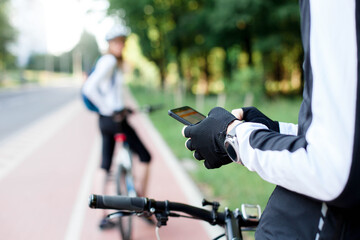 Cyclist using map app with navigation on mobile phone. Couple riding bikes on town street. Road with bicycle path in park. Healthy lifestyle. Outdoors activities with social distancing. Local travel.