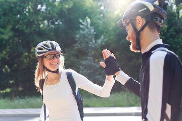 Man and woman in protective bicycle helmets give each other high five after successful sport training. Happy couple riding bikes outside. Healthy lifestyle. Outdoors activities and fun in new normal.