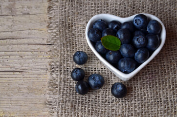 Freshly picked organic blueberries in a white heart shaped bowl on wooden background.Blueberry. Bilberries.Healthy eating,vegan food or diet concept with copy space.