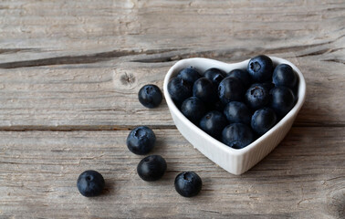 Freshly picked organic blueberries in a white heart shaped bowl on old wooden background.Blueberry. Bilberries.Healthy eating,vegan food or diet concept with copy space.