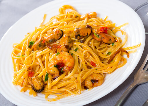Image of delicious pasta of shrimps, mussels and greens at plate