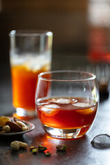 2 glasses of whisky with ice on dark background.  Accessorised with dish of nuts and decorative drinks tray in background