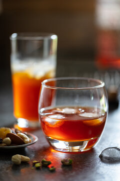 2 glasses of whisky with ice on dark background.  Accessorised with dish of nuts and decorative drinks tray in background