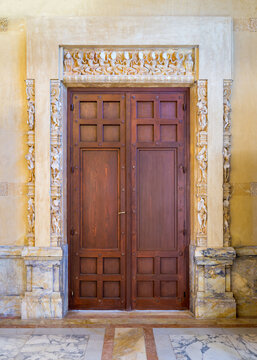 Closed elegant lumber door installed in ornamental archway outside of old marble building