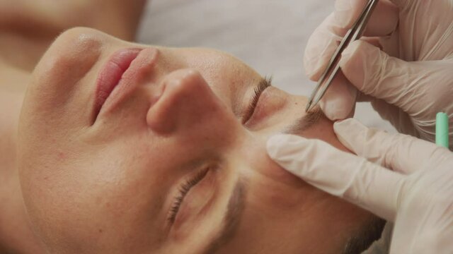 Tweezing eyebrows, portrait of client while cosmetological procedure, self-care routine while quarantine