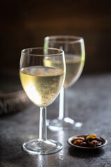 2 glasses of chilled white wine with dish of nuts on dark bar.  Out of focus drinks tray in background. Simple presentation