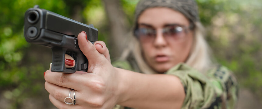 Attractive soldier woman practice shooting and gun point aim to attacker. Close-up pistol pointing front view. Nature outdoor