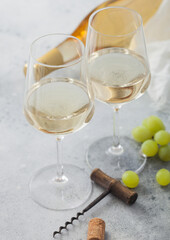 Two glasses of white homemade summer refreshing wine with grapes and corkscrew and bottle on light...