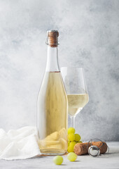 Glass and bottle of white homemade wine with grapes and corkscrew with linen cloth on light...