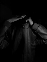 Man without face wearing leather jacket on a dark background. His hand is placed where his head...