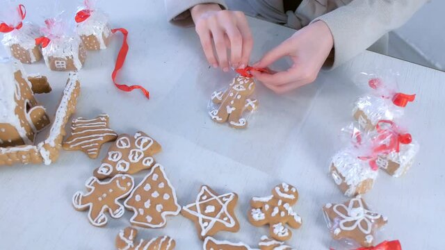 Woman packaging funny gingerbread man cookie with icing for Christmas, top view, hands closeup. Preparing presents, gifts in New Year time. Homemade sweet bakery. Gingerbread house.