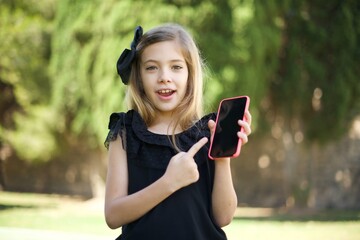 Excited woman pointing with finger at digital device. Studio shot of shocked girl holding smartphone with blank screen.